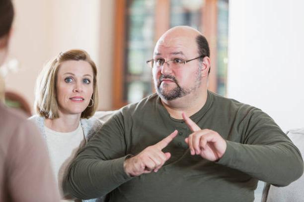 Man using signing to communicate with a person off camera. A woman standing behind him looking at the same person